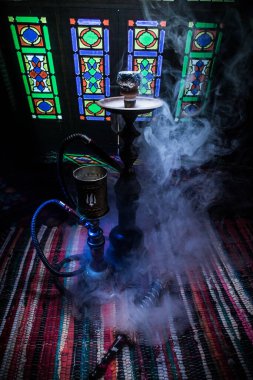 Shisha kasesinde sıcak nargile kömürleri Arap iç kısımlarında buhar bulutları oluşturuyor. Halıdaki doğulu süsü. Karanlıkta arka planda şık bir doğulu shisha..