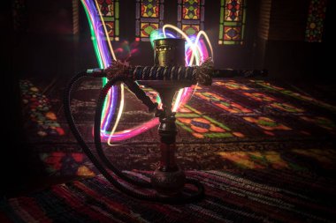Shisha kasesinde sıcak nargile kömürleri Arap iç kısımlarında buhar bulutları oluşturuyor. Halıdaki doğulu süsü. Karanlıkta arka planda şık bir doğulu shisha..