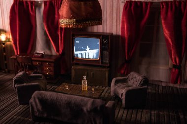 Geceleri mobilyası ve penceresi olan gerçekçi bir bebek evi oturma odası. El yapımı gerçekçi bebek eviyle sanat masası dekorasyonu. Eski usul televizyon. Seçici odak.