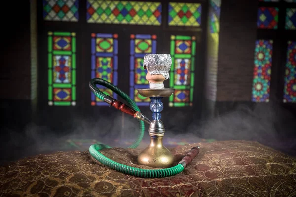 Hookah hot coals on shisha bowl making clouds of steam at Arabian interior. Oriental ornament on the carpet. Stylish oriental shisha in dark with backlight.