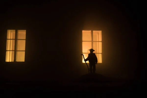 Old house with a Ghost in the forest at night. Horror silhouette at the window. Horror Halloween concept Alone man silhouette standing near window of dollhouse at night. Selective focus