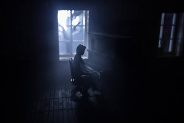 Geceleri mobilyası ve penceresi olan gerçekçi bir bebek evi oturma odası. Karanlık odada eski piyanonun başında oturan adam. Seçici odak.
