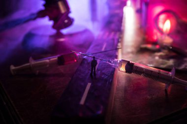 Narcotic drug problem concept. Silhouette of a man standing in the middle of the road on a misty night with giant Drug syringe and narcotic attributes. Creative artwork decoration