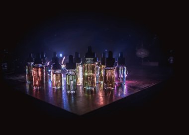 Vape konsepti. Karanlık arka planda duman bulutları ve tüp sıvısı şişeleri. Işık efektleri. Arka plan, vape reklamı ya da vape arkaplan olarak kullanışlı. Seçici odak