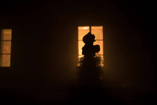 Old house with a Ghost in the forest at night. Horror silhouette at the window. Horror Halloween concept Alone woman silhouette standing near window of dollhouse at night. Selective focus