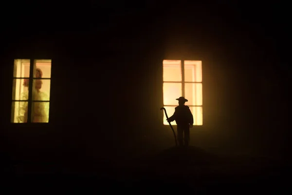 Old house with a Ghost in the forest at night. Horror silhouette at the window. Horror Halloween concept Alone man silhouette standing near window of dollhouse at night. Selective focus