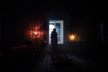 Geceleri mobilyası ve penceresi olan gerçekçi bir bebek evi oturma odası. Pencerede oturan romantik bir çift. El yapımı gerçekçi bebek eviyle sanat masası dekorasyonu. Seçici odak.