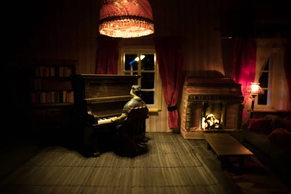 A realistic dollhouse living room with furniture and window at night. Man sitting at the old piano in dark room. Selective focus.