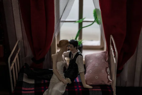 A realistic dollhouse bedroom with furniture and window at night. Romantic couple sitting on window. Man and woman making love in bedroom. Artwork table decoration . Selective focus.