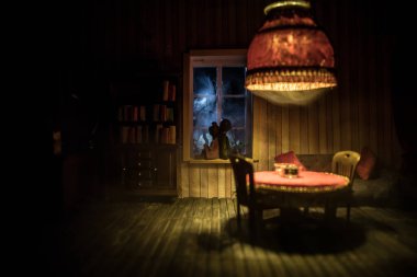 Geceleri mobilyası ve penceresi olan gerçekçi bir bebek evi oturma odası. Pencerede oturan romantik bir çift. El yapımı gerçekçi bebek eviyle sanat masası dekorasyonu. Seçici odak.