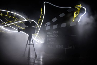 Movie concept. Miniature movie set on dark toned background with fog and empty space. Silhouette of vintage camera on tripod and clapboard. Selective focus clipart