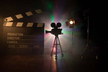 Film konsepti. Sis ve boşluk ile koyu tonlu arkaplanda minyatür film seti. Tripod ve klasördeki klasik kamera silueti. Seçici odak