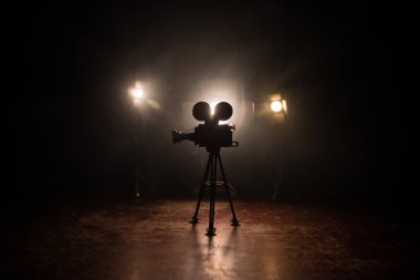 Film konsepti. Sis ve boşluk ile koyu tonlu arkaplanda minyatür film seti. Tripodun üzerinde klasik kamera silueti. Seçici odak