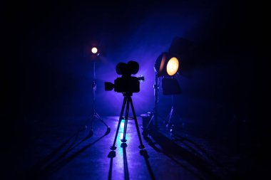 Film konsepti. Sis ve boşluk ile koyu tonlu arkaplanda minyatür film seti. Tripodun üzerinde klasik kamera silueti. Seçici odak