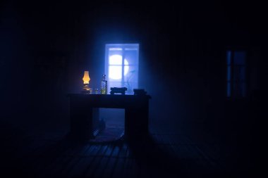 Geceleri mobilyası ve penceresi olan gerçekçi bir bebek evi oturma odası. Karanlık odada masada oturan bir adam. Küresel virüs salgını sırasında evde kalma kavramı. Seçici odak.