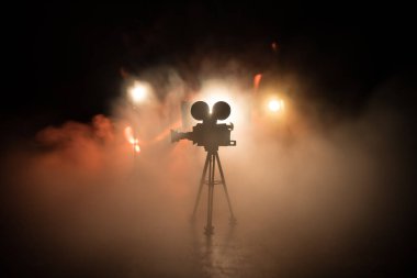 Film konsepti. Sis ve boşluk ile koyu tonlu arkaplanda minyatür film seti. Tripodun üzerinde klasik kamera silueti. Seçici odak