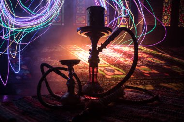 Shisha kasesinde sıcak nargile kömürleri Arap iç kısımlarında buhar bulutları oluşturuyor. Halıdaki doğulu süsü. Karanlıkta arka planda şık bir doğulu shisha..