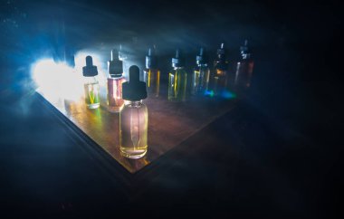 Vape konsepti. Karanlık arka planda duman bulutları ve tüp sıvısı şişeleri. Işık efektleri. Arka plan, vape reklamı ya da vape arkaplan olarak kullanışlı. Seçici odak