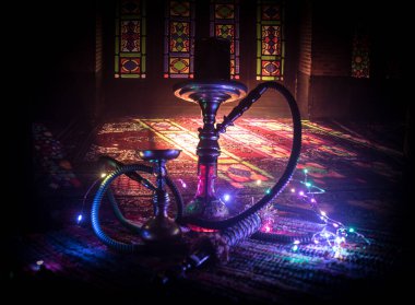 Shisha kasesinde sıcak nargile kömürleri Arap iç kısımlarında buhar bulutları oluşturuyor. Halıdaki doğulu süsü. Karanlıkta arka planda şık bir doğulu shisha..