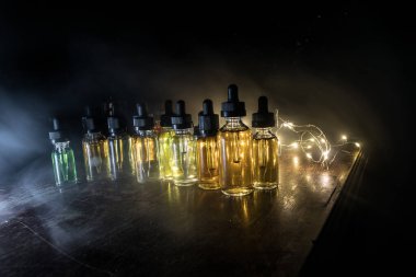 Vape konsepti. Karanlık arka planda duman bulutları ve tüp sıvısı şişeleri. Işık efektleri. Arka plan, vape reklamı ya da vape arkaplan olarak kullanışlı. Seçici odak