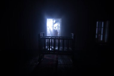 Karanlık odanın penceresinin yanındaki ürkütücü bebek karyolası. Karanlıktaki korkunç bebek silueti. Geceleri mobilyası ve penceresi olan gerçekçi bir bebek evi oturma odası. Seçici odak