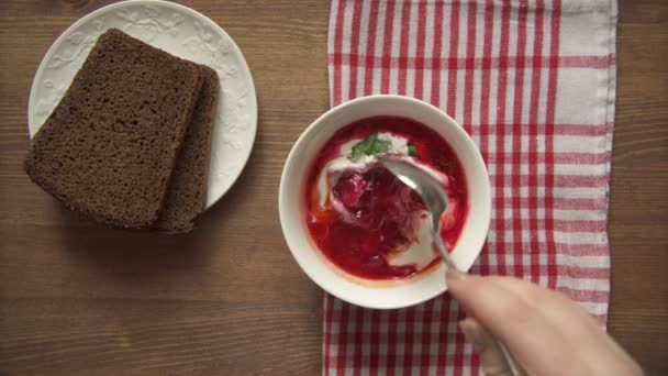 La mano femenina pone hueso en el plato y toma otro trozo de carne asada. La chica revuelve un plato de borsch — Vídeos de Stock