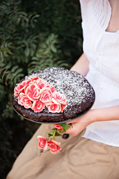 A young women sitting in a garden with chocolate cake and red flowers. Romantic mood — Stock Photo, Image