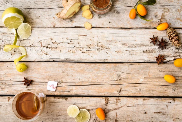 Hot tea, spices, lemon, oranges, cone and ginger root on a wooden background. Winter still life. Up view. Copy space for your text. — Stock Photo, Image