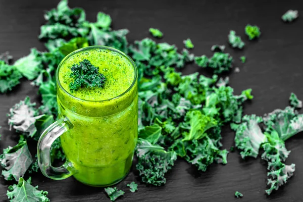 Healthy smoothie with green kale leaves in a glass on black background