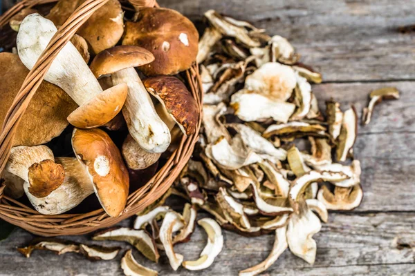 Frische Steinpilze im Korb und trockene Pilze auf Holztisch, über Kopf — Stockfoto