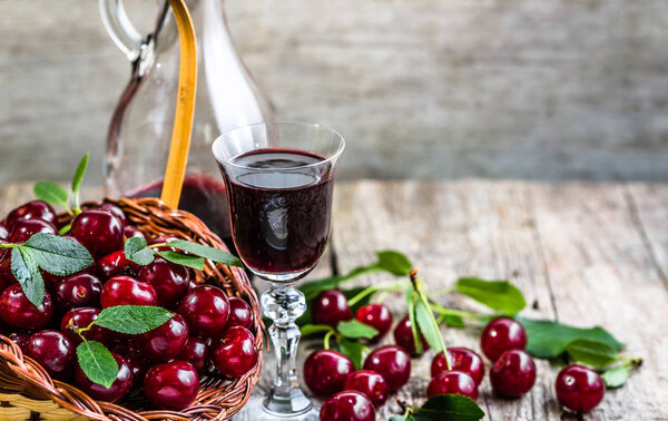 Glass of cherry tincture, healthy liquor in a bottle on rustic wooden background