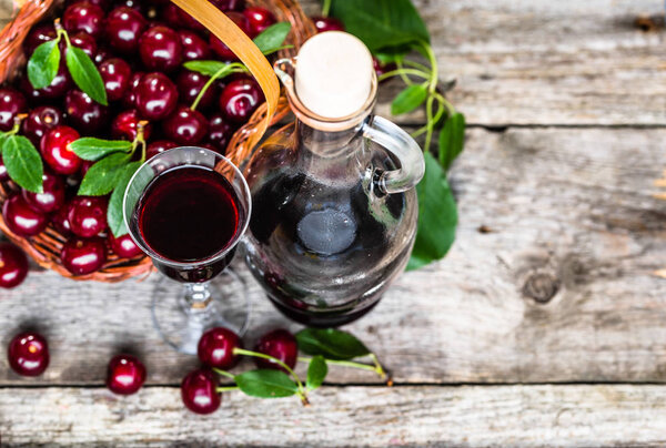 Glass of alcohol tincture made from cherry fruits, liquor in a bottle on rustic background