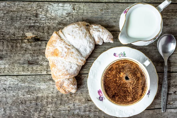 Вкусный десерт - круассан и чашка кофе на деревянном столе сверху — стоковое фото