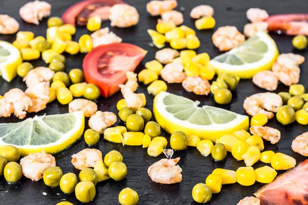 Colorato sfondo vegetale o mediterraneo con gamberetti, pomodoro, mais e fette di limone su piatto nero — Foto Stock