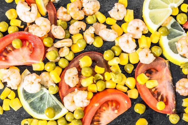 Fondo colorido de la cocina vegetal o mediterránea con camarones, tomate, maíz y rodajas de limón en plato negro, puesta plana — Foto de Stock