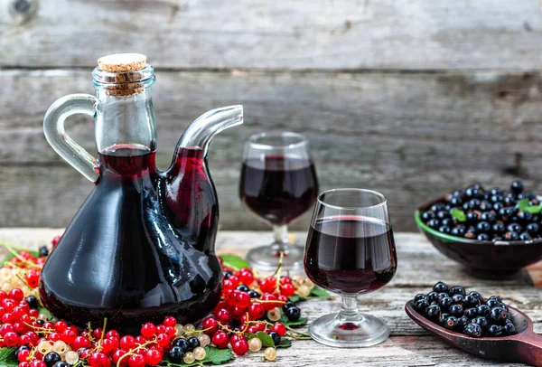 Старый винный графин на деревянном столе. Сладкий алкоголь из фруктов много различных ягод смородины — стоковое фото