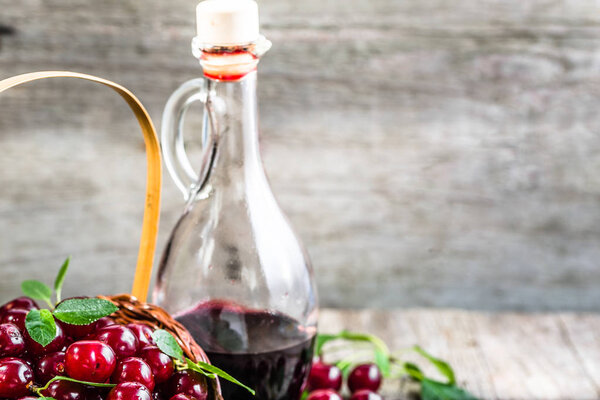 Cherry wine in a glass bottle on wooden table. Sweet alcohol made from cherry fruits