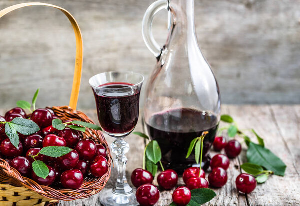 Glass of wine and vintage glass bottle on wooden table. Sweet alcohol made from cherry fruits