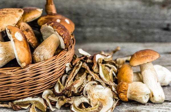 Getrocknete Pilze und frisch geerntete Steinpilze in einem Korb auf rustikalem Holzgrund — Stockfoto