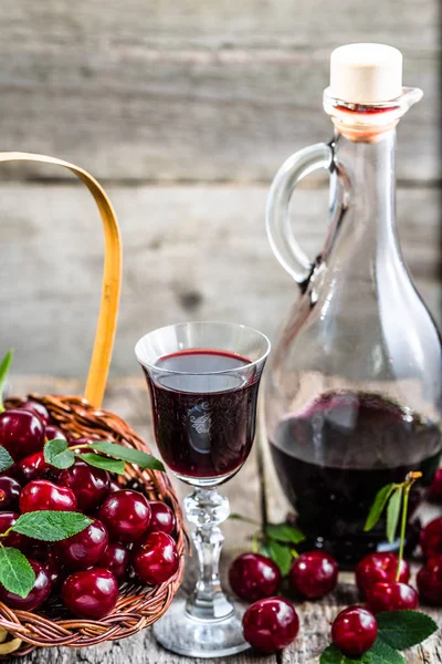 Стакан ликера с вишневыми фруктами и бутылкой деревенского вина, настойка домашнего спирта на деревянном столе — стоковое фото