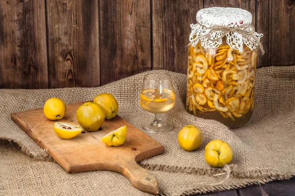 Tintura de membrillo en un frasco de vidrio y frutas frescas de membrillo en una mesa de madera —  Fotos de Stock