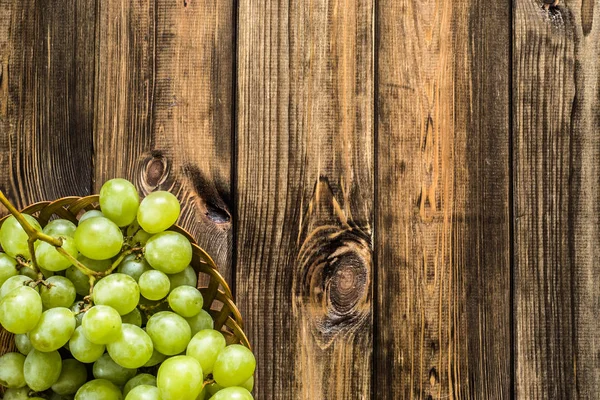 Ramo de uvas verdes en la cesta, frutas de otoño sobre fondo de madera —  Fotos de Stock