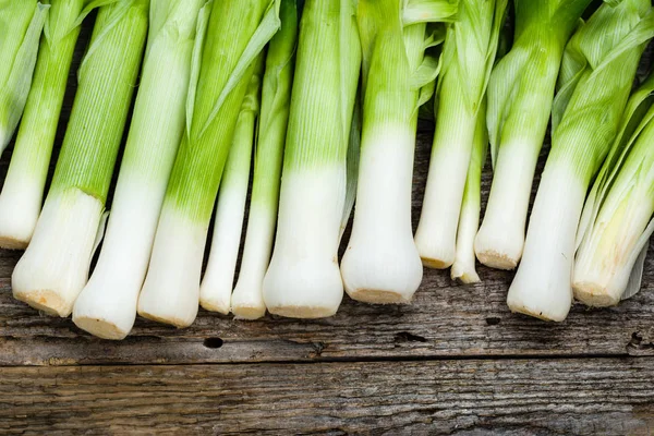 Harvest of leeks, green vegetables, local market produce on rustic wooden farm table, overhead