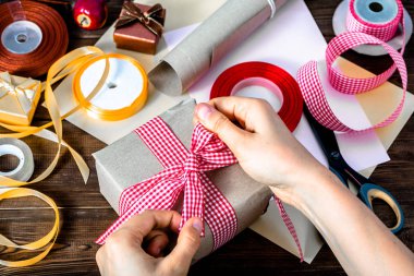 Wrapping christmas present with gray paper and ribbons. Hands making bow on gift. clipart