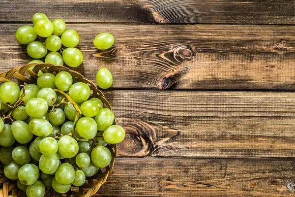 Cambada de uvas verdes na cesta, frutos do outono em fundo de madeira — Fotografia de Stock