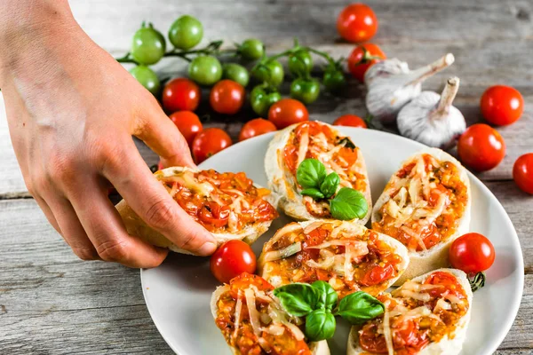 Ruka jí předkrm nebo Italská bruschetta s rajčaty, bazalkou a sýrem, oběd na stole, finger food koncept — Stock fotografie