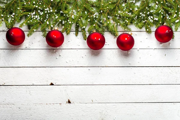 Χριστουγεννιάτικη διακόσμηση, στα σύνορα με κόκκινες μπάλες πάνω σε κλαδιά έλατου και νιφάδες χιονιού σε άσπρο φόντο ξύλινη — Φωτογραφία Αρχείου