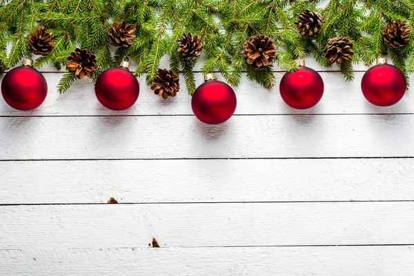 Çam dalları üzerinde kırmızı topları ve Beyaz ahşap zemin üzerinde kar taneleri ile şenlikli Noel sınır