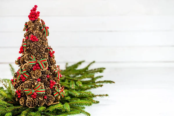 Сосновый конус рождественская елка фон с красным Холли и ель на белой деревянной доске — стоковое фото