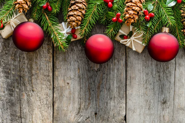 Noel hediye kutuları ve dekorasyon - kırmızı süsler, çam kozalakları ve holly ahşap tahta üzerinde çam dalları üzerinde arka plan